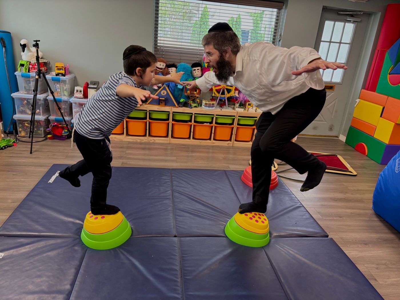 A father and son balancing on stepping stones together, arms out, on the gym mats