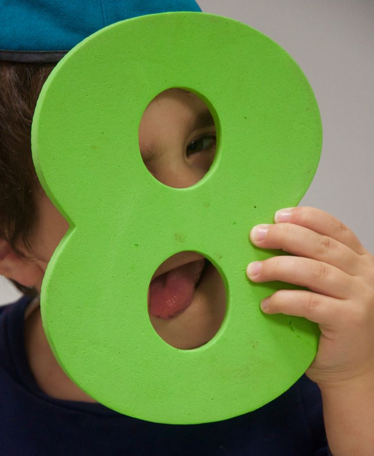 A child peeking through a foam number eight with his tongue out