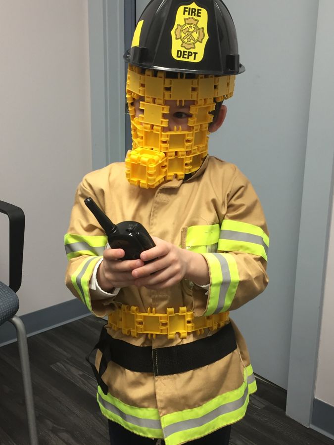 A child dressed as a firefighter with a mask made of building pieces
