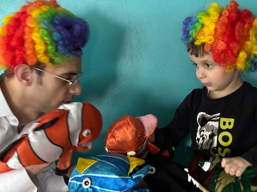 A clinician and child in rainbow wigs playing with fish puppets